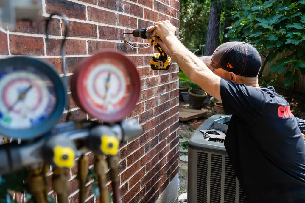 A Cover HVAC technician working at an outdoor condenser with refrigerant manifold gauges in the foreground