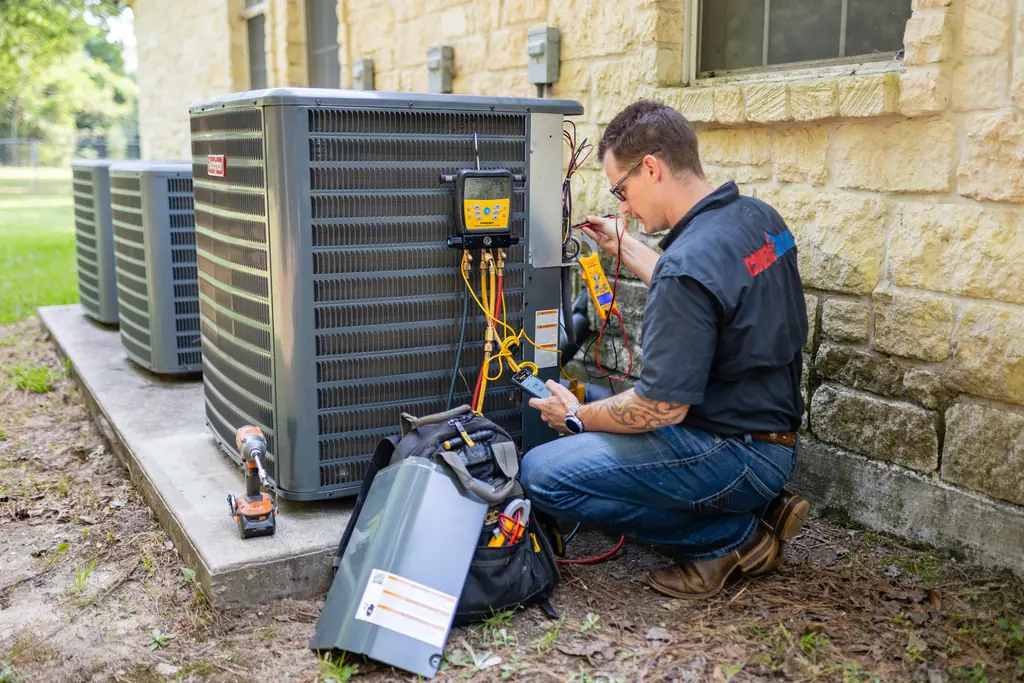 A Cover HVAC technician taking readings at a bank of outdoor condensers with a digital manifold and a clamp meter